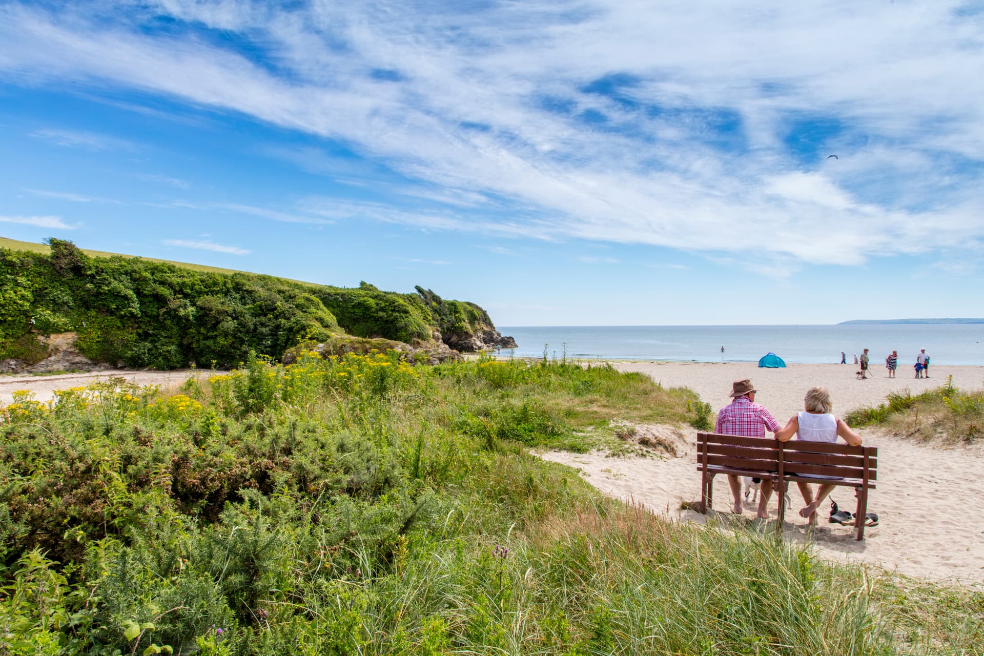 Couple sitting on a bench overlooking a sandy beach in Cornwall